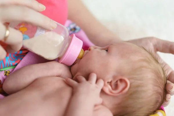 A small newborn girl is fed formula from a bottle in her mothers arms. Artificial feeding