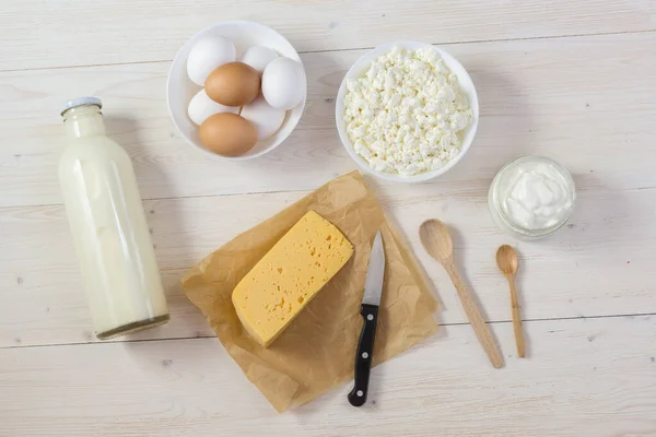 Fresh calcium-rich dairy products-cottage cheese, sour cream and cheese, as well as eggs are laid on a white wooden table. Natural and healthy food