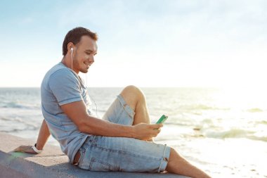 okyanus yakın oturan hareket eden smartphone ile yakışıklı adam