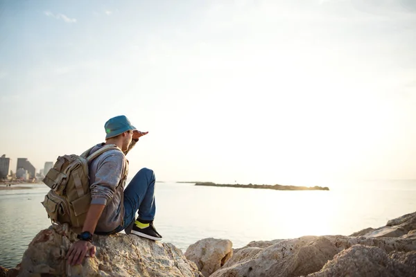 Resenär med ryggsäck sitter på klipporna nära havet — Stockfoto