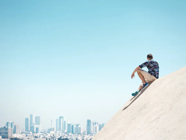 Man sitting on a cliff and looking at the city — Stock Photo, Image