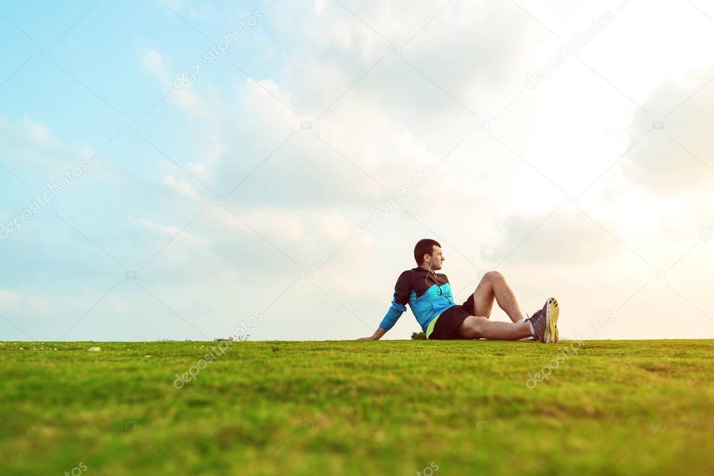 sportsman resting after sport in the park and looking far away at the sunset