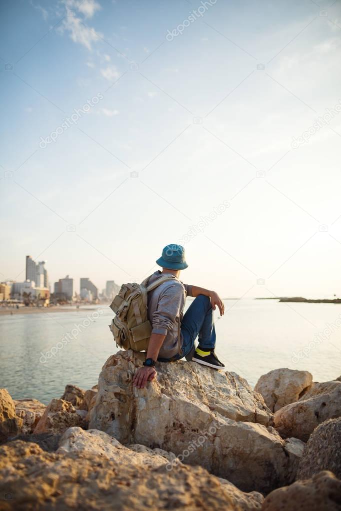 traveler with backpack sitting on the rocks near the sea