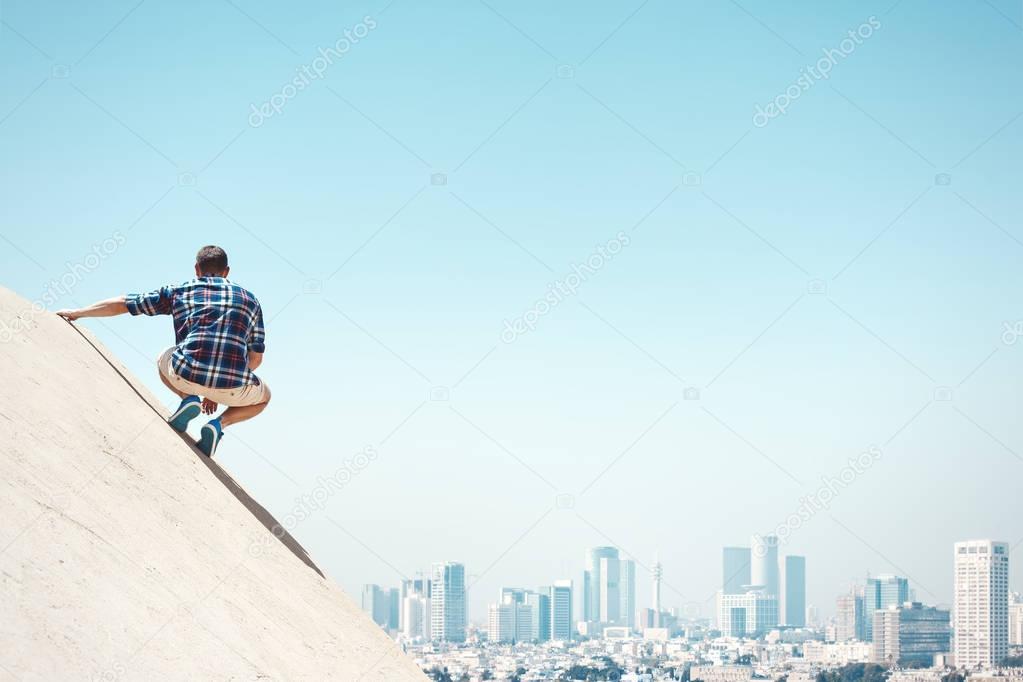 man sitting on a cliff and city