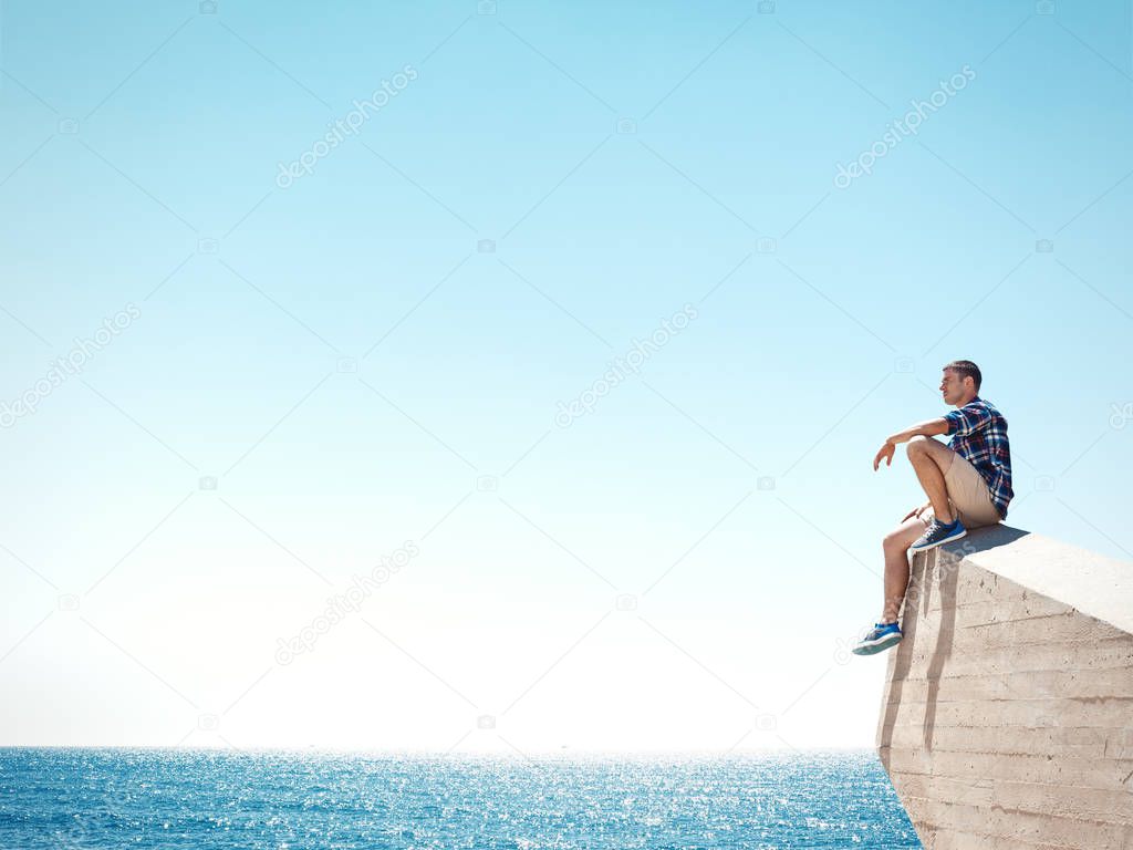 man sitting on a cliff and looking at the sea