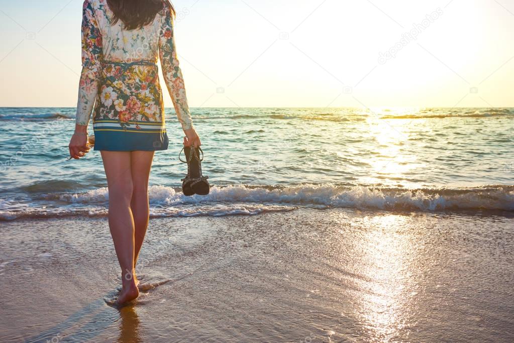beautiful woman in colorful dress standing on the beach near the ocean and looking far away at the sunset