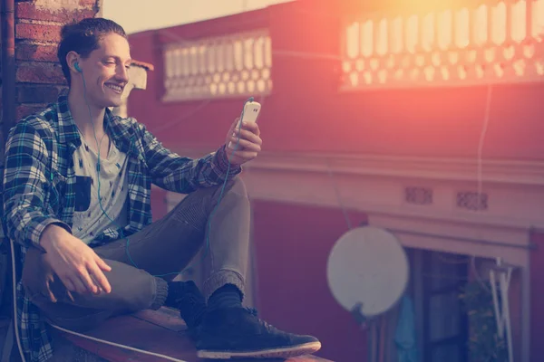 Smiling man sitting on the roof with mobile phone and listening music