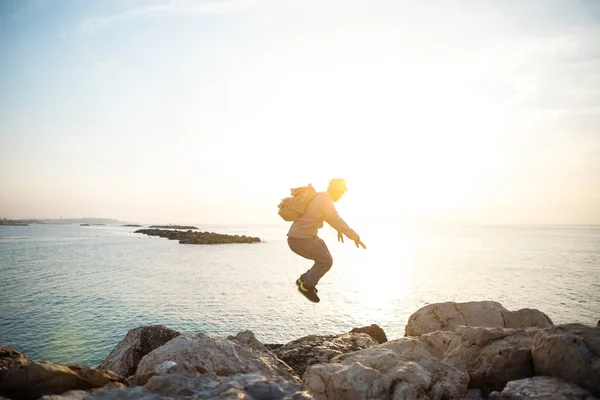 Uomo con zaino saltando sopra le rocce — Foto Stock