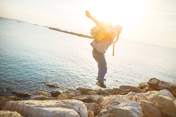 храбрый человек с рюкзаком прыгает через скалы
