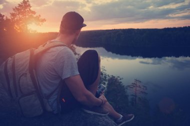 Casual adam yukarıda nehir ve uzakta seyir uçurumun kenarında oturan sırt çantası ile