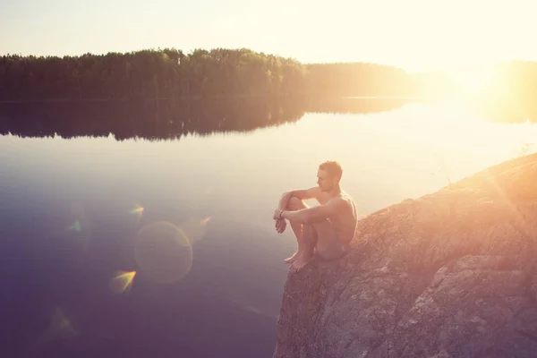 man sitting on the edge of the cliff near the lake after swimming
