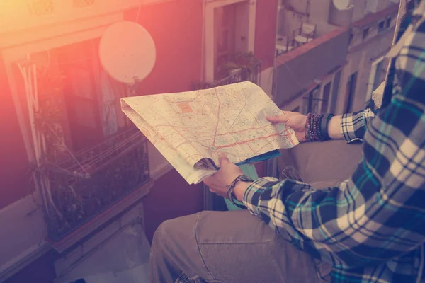 Young man sitting on the edge of high roof with map in hands