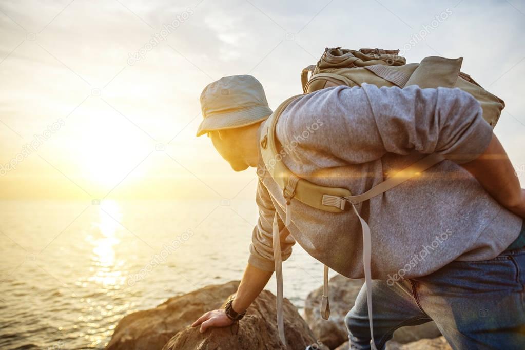 traveling man with backpack near the ocean looking far away