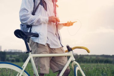 Tablet bilgisayar ile yeşil alanda bisiklet ile genç adam