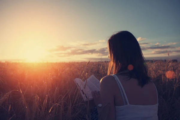 Young handsome girl reading book outdoors in sunset in the field — Stock Photo, Image