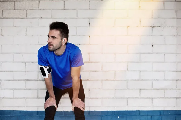 Athlète masculin fatigué avec écouteurs reposant près du mur blanc de brique — Photo