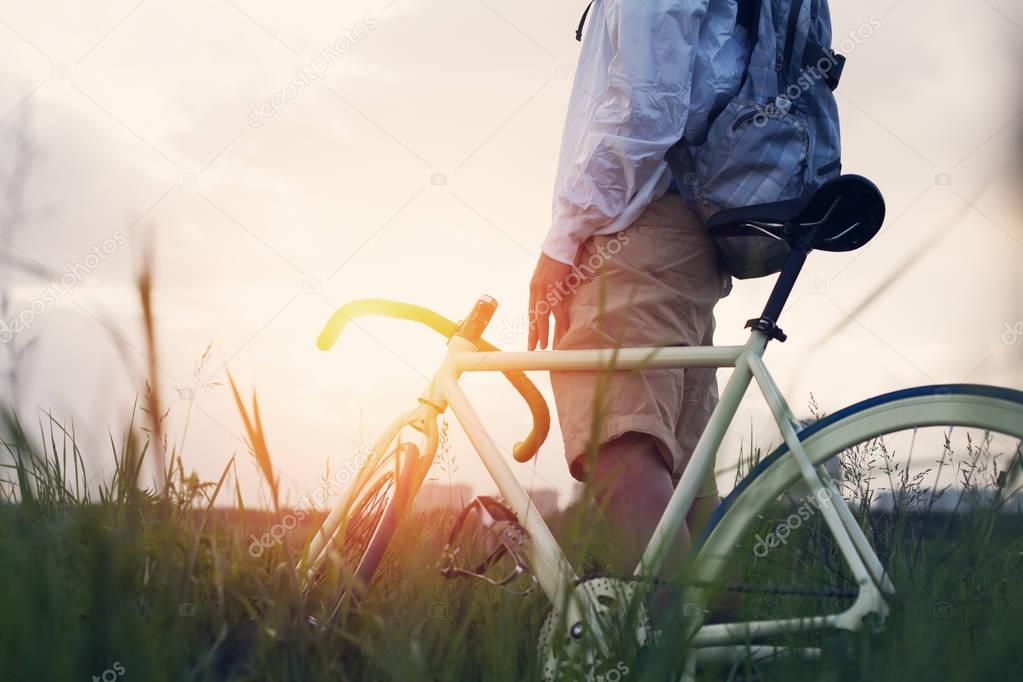 Young man with bicycle in the green field at sunset