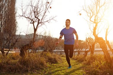 Yakışıklı genç atlet (küçük mot gün batımında parkta koşu