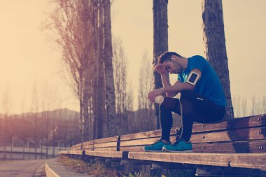 Şişe ile parkta bankta oturan yorgun terli atlet