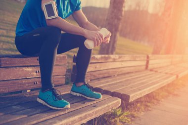 Şişe su ile parkta bankta oturan yorgun atlet 