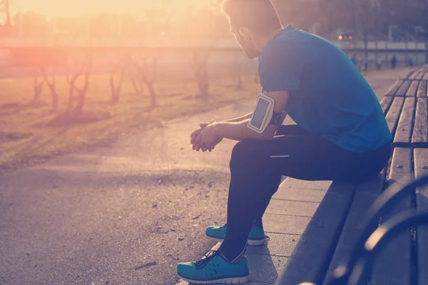 Чоловік-спортсмен відпочиває на лавці в парку на заході сонця після бігу — стокове фото