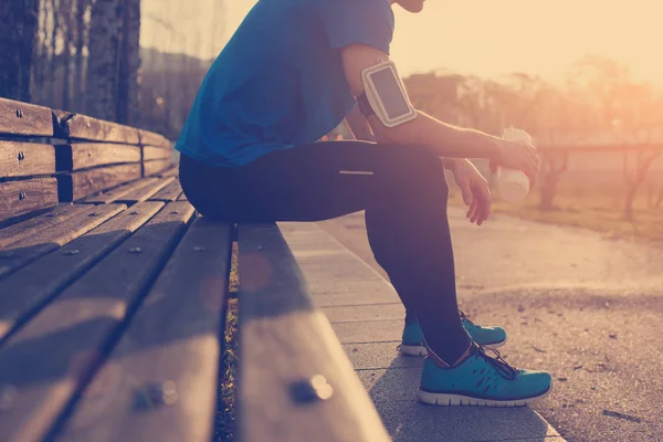 Atleta descansando no banco no parque ao pôr do sol depois de correr com bo — Fotografia de Stock