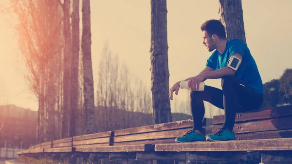 Trött idrottsman vilar på bänken i parken med flaska vatten, — Stockfoto