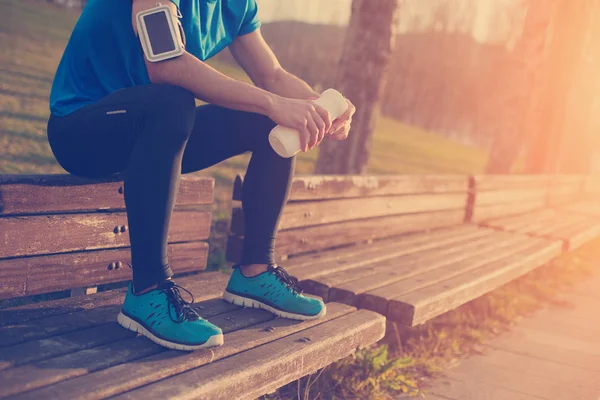 Şişe su ile parkta bankta oturan yorgun atlet 