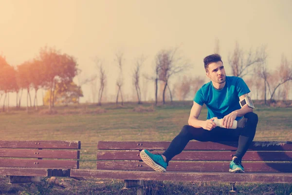 Beau athlète reposant sur le banc dans le parc avec bouteille de wat — Photo