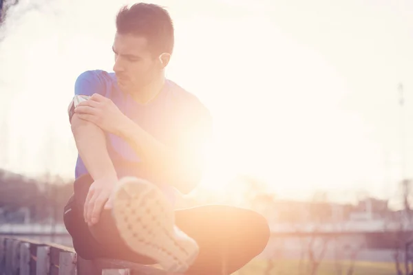 Athlete sitting in the park at sunset touching armband with mobi — Stock Photo, Image