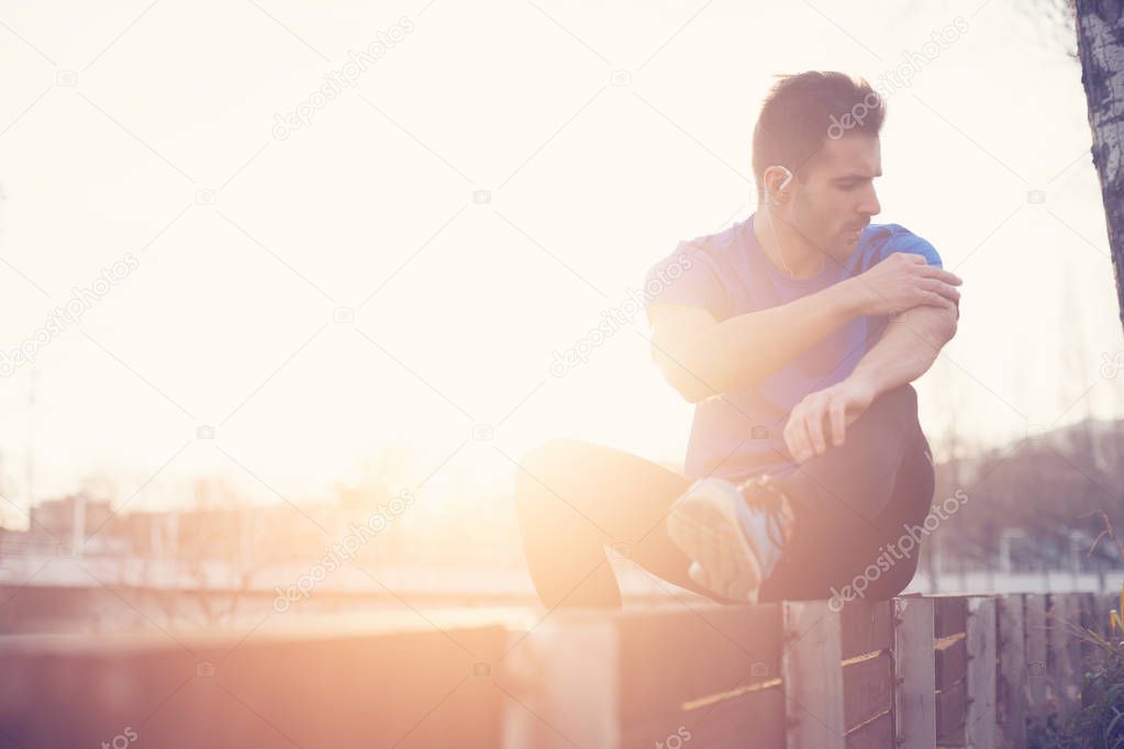 Athlete sitting in the park at sunset touching mobile phone (int