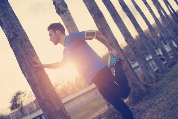 Atleta masculino preparando pernas para correr no parque ao pôr do sol (i — Fotografia de Stock