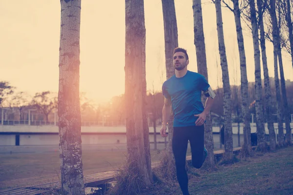 Atleta bonito correndo no parque ao longo de árvores ao pôr do sol (litt — Fotografia de Stock