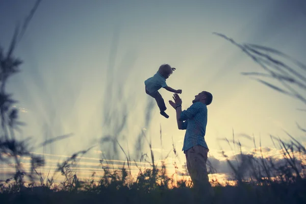 Silhouette of father throwing up his son in the park — Stock Photo, Image