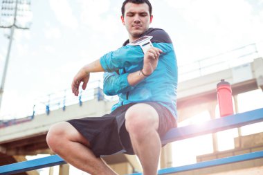 şişe su ve stadyum korkuluk üstünde hareket eden telefon ile oturan sporcu