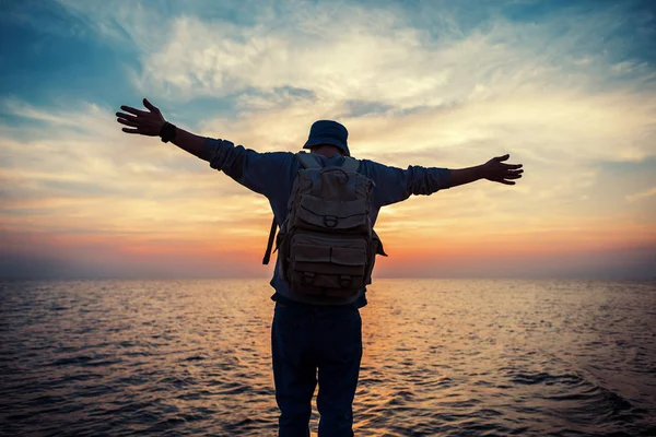 Traveler with backpack and outspread hands near sea at sunset — Stock Photo, Image