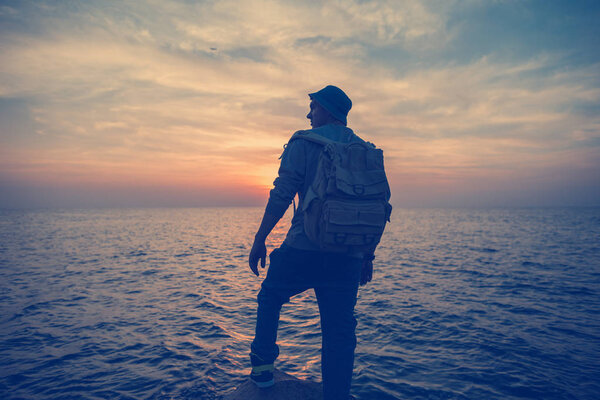 traveler with backpack near sea looking far away at horizon at sunset (intentional vintage color)