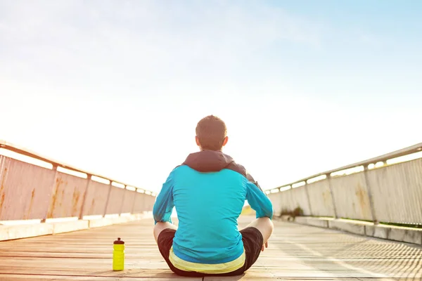 Sportif sportif avec une bouteille d'eau assis et reposant sur le sol en bois dans le parc — Photo