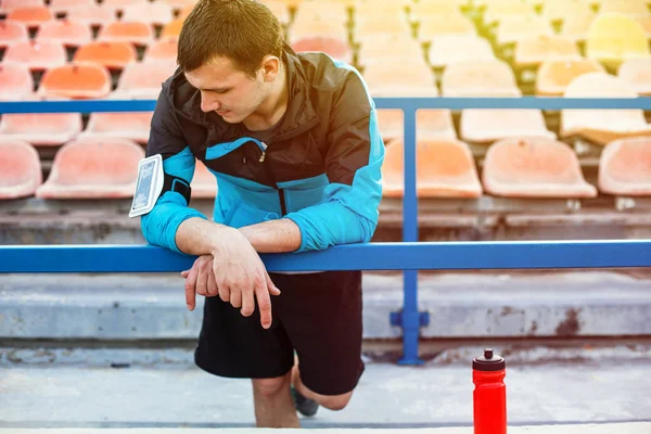 Sportler steht mit Wasserflasche und Handy am Geländer am Stadion — Stockfoto