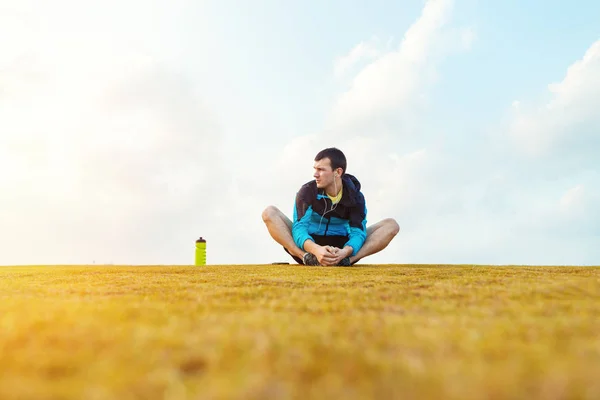 Sportsman with a bottle of water sitting and doing warming stretching exercise in the park — Stock Photo, Image