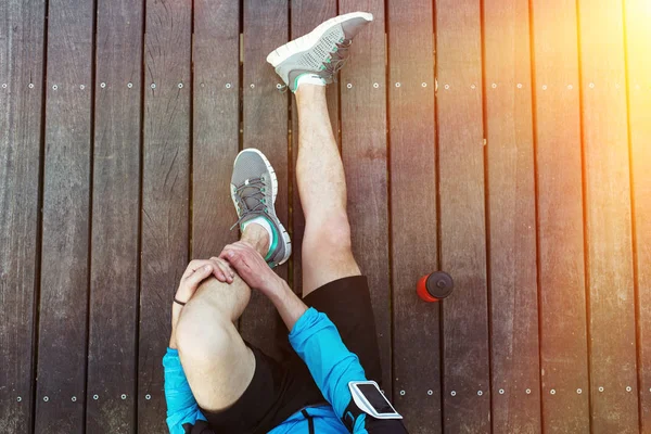 Descansando pernas de desportista sentado no chão de madeira com garrafa de plástico esporte vermelho, vista do topo — Fotografia de Stock