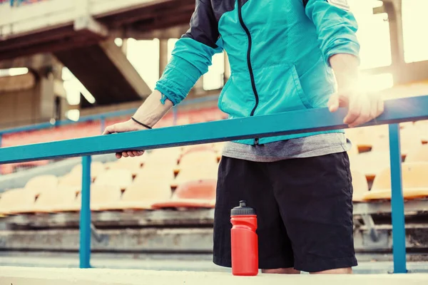 Κουρασμένος αθλητής με μπουκάλι νερό που αναπαύεται στο κιγκλίδωμα στο στάδιο — Φωτογραφία Αρχείου
