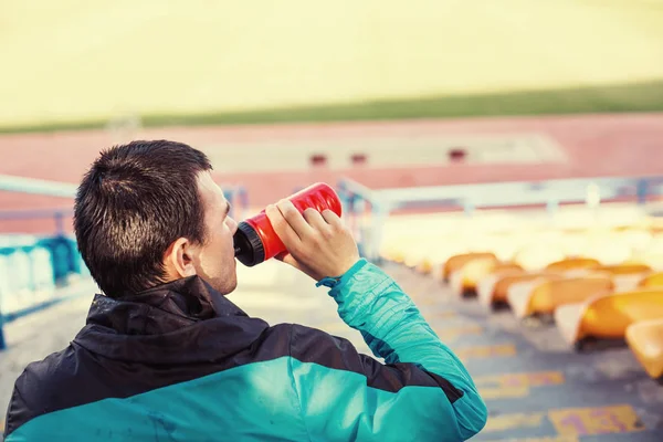 tired sportsman drinking water at stadium