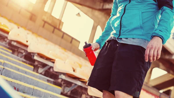 Sportman met rode fles water staande op het stadion — Stockfoto