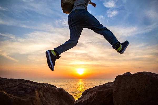 Reisender springt bei schönem Sonnenuntergang über Felsen am Meer Stockbild