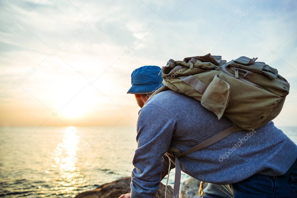 traveler with backpack on the rocks near the sea looking far away at horizon