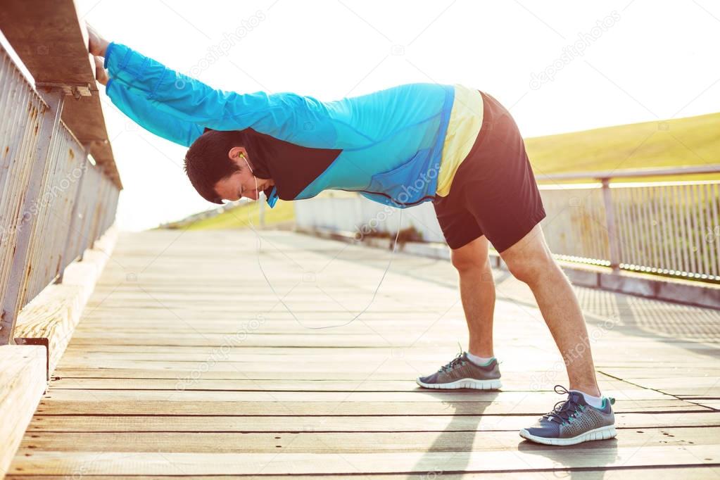 athletic sportsman doing warming stretching exercise in the park