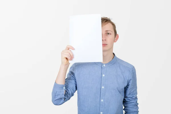Серйозний хлопчик-підліток тримає чистий аркуш паперу, що покриває половину — стокове фото