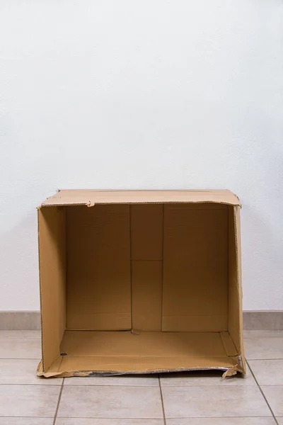 Open empty cardboard box on the floor inside a room with copy sp — Stock Photo, Image