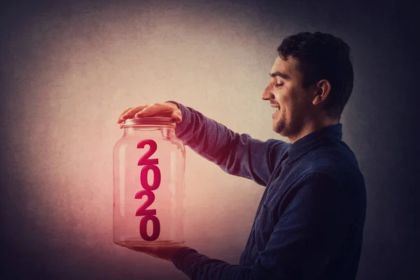 Радісний молодий чоловік відкриває кришку скляної банки з червоним 2020 нюансом — стокове фото